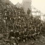 Miners pose with lunch pails in hand on a mine rock pile outside of the Tamarack mineshaft.